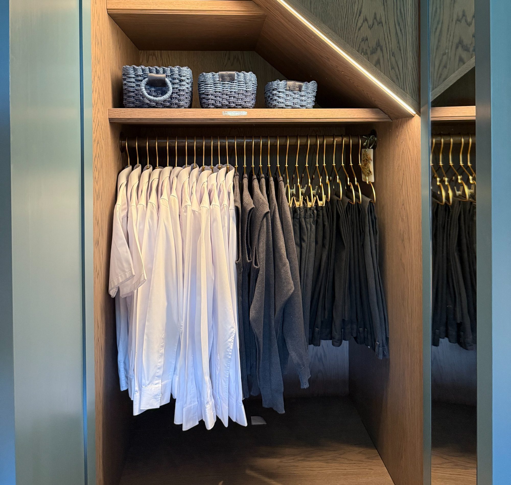Shirts hung in a wardrobe beneath baskets on a shelf.