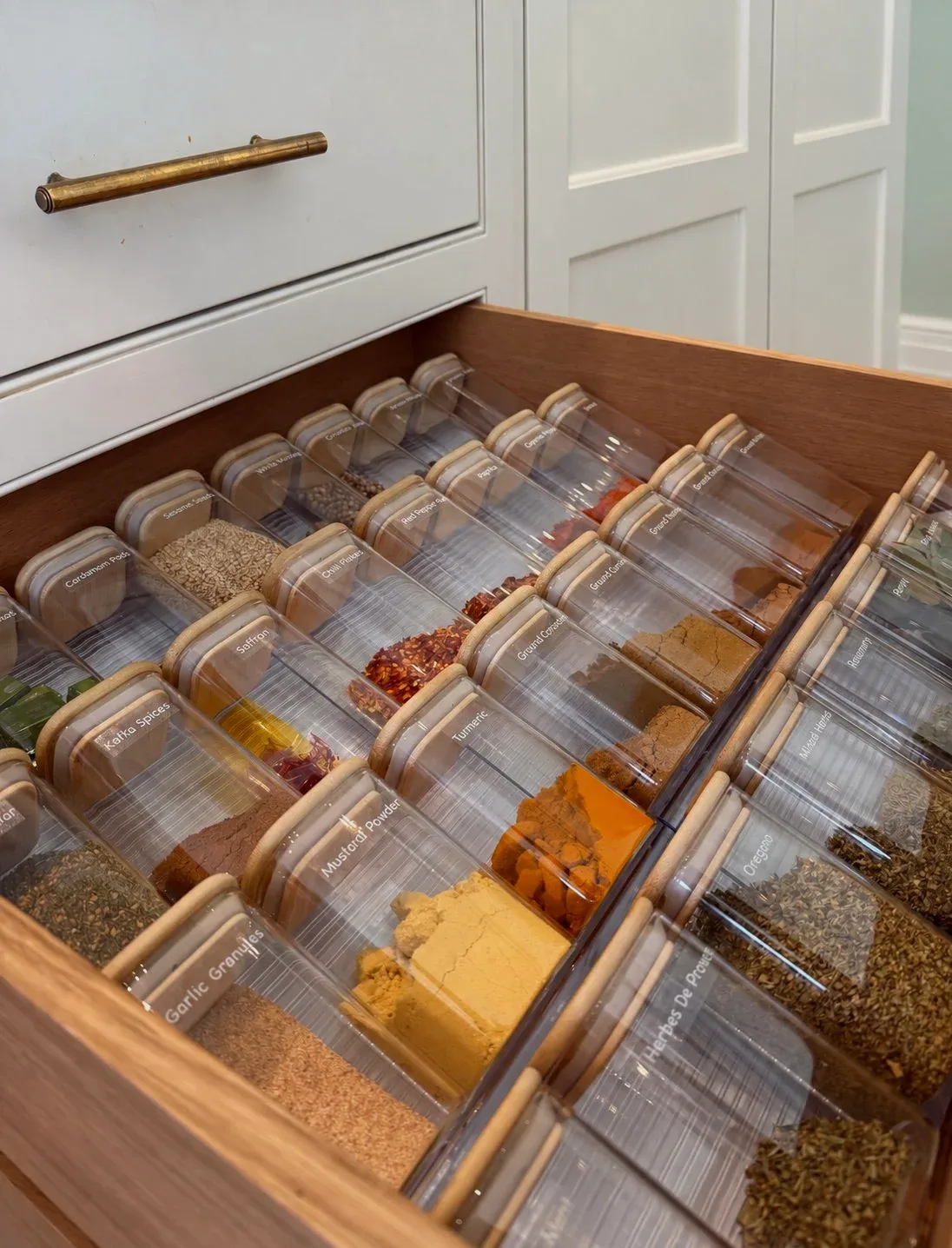 A drawer of spice jars laid flat in timber dividers.