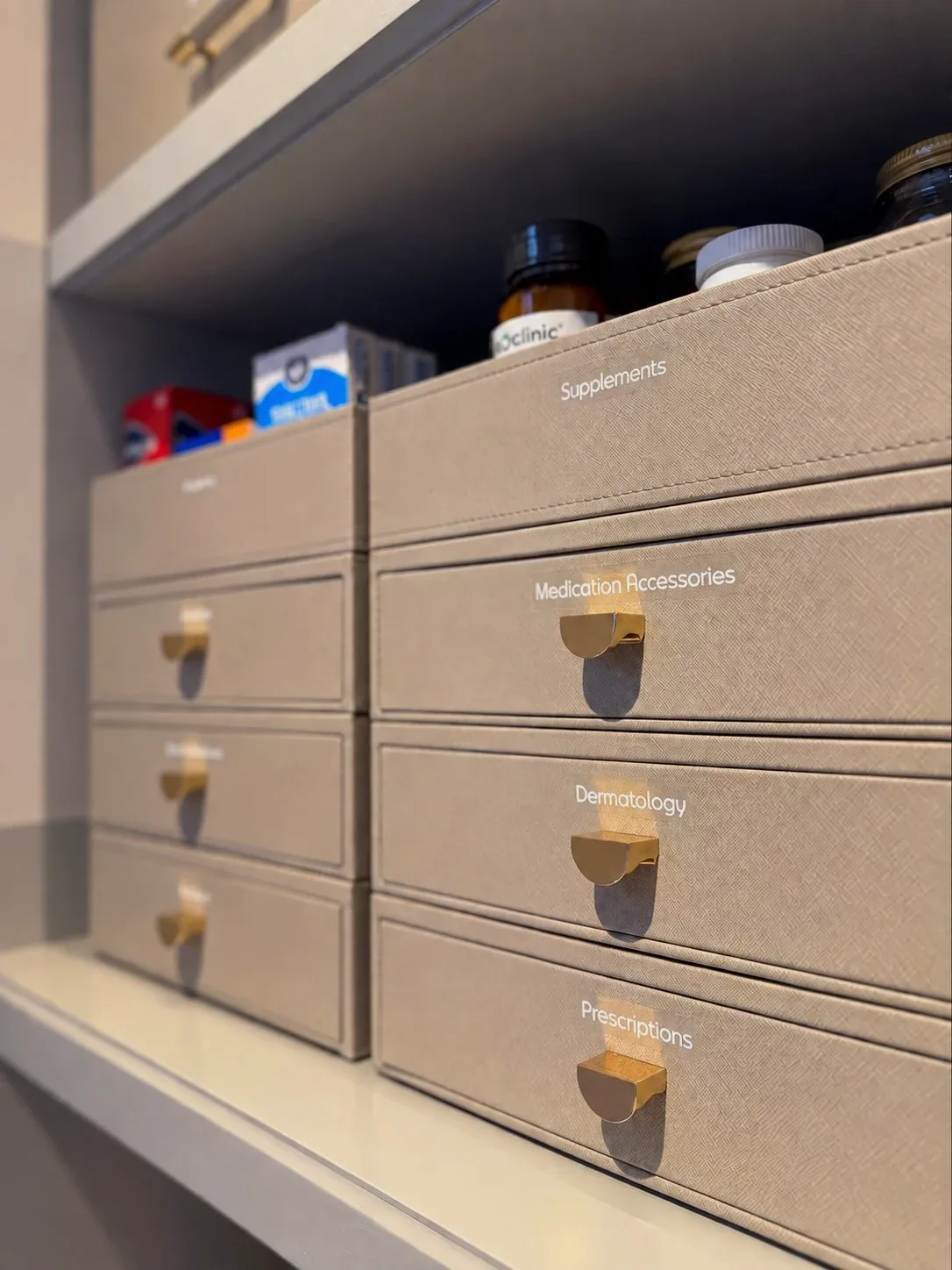 Stacked linen drawer boxes with brass pulls, labelled for supplements, dermatology and prescriptions.