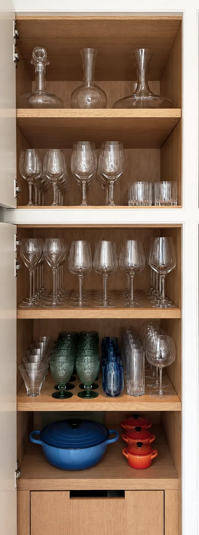 Wine glasses and tumblers on the shelves of a tall cabinet.