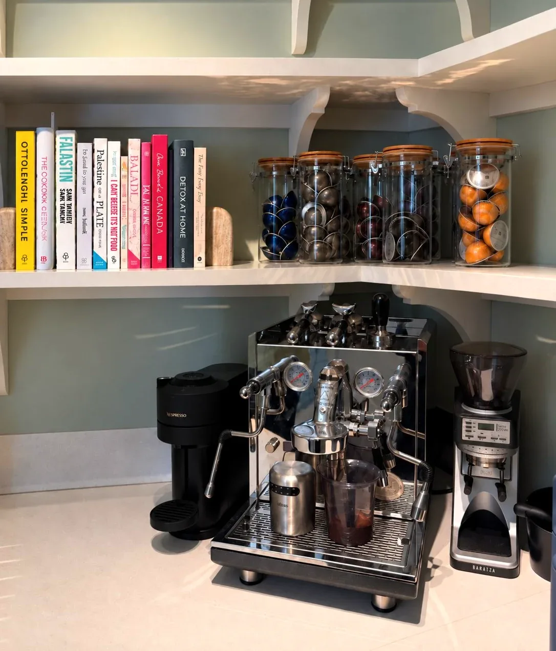 A coffee machine on a worktop, cookery books on the shelf above.
