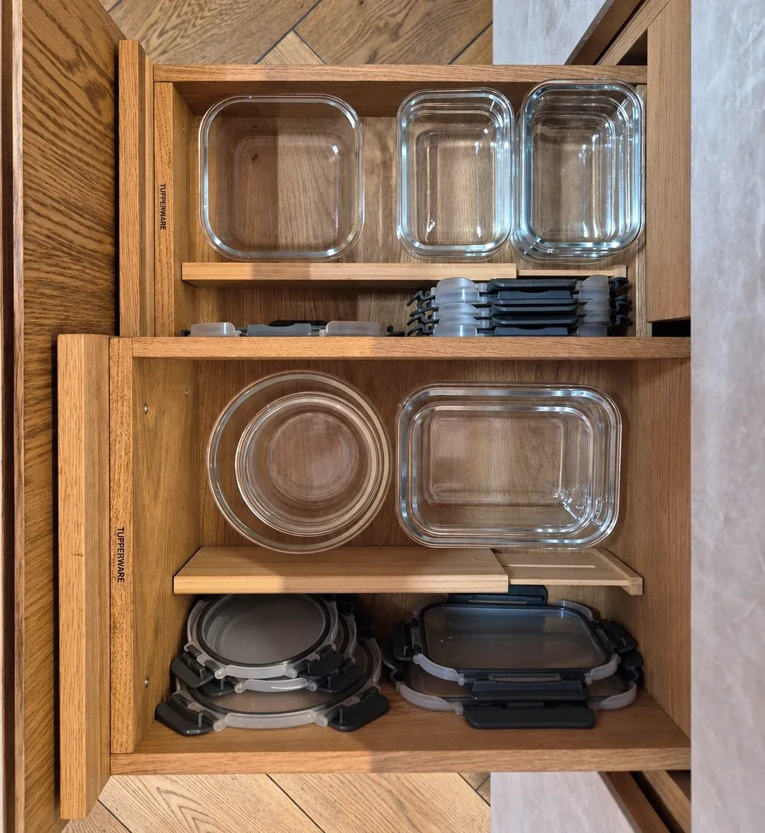 Glass food containers and their lids on pull-out timber shelves.