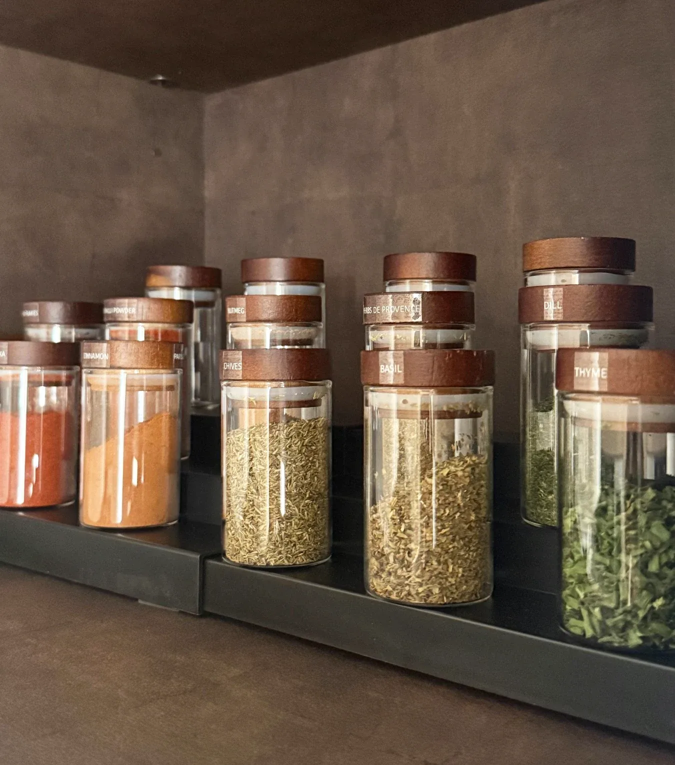 Spice jars with copper lids ranged along a dark pantry shelf.