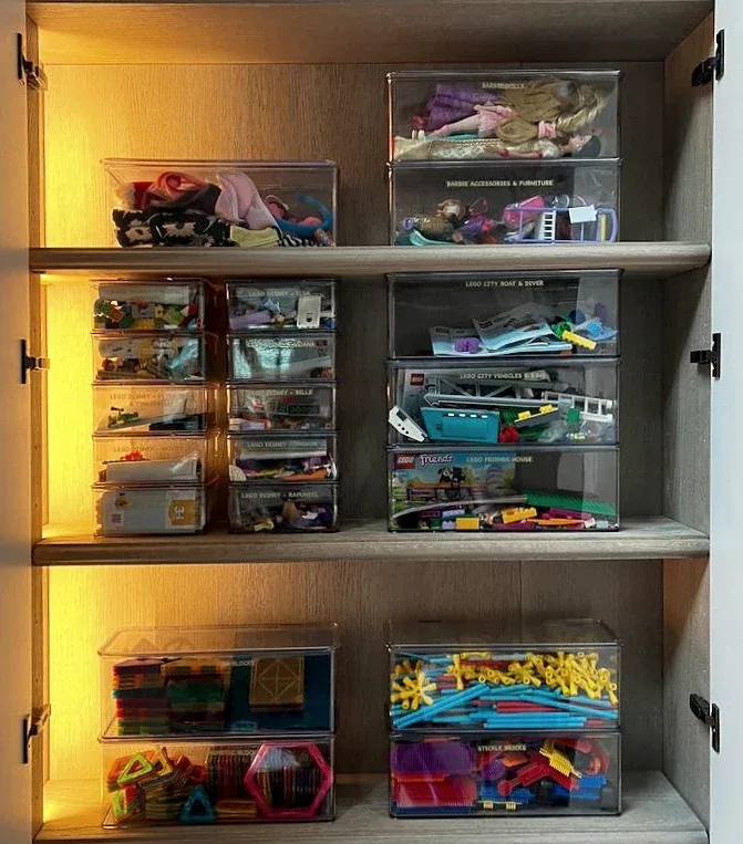 A lit cabinet of clear trays holding craft materials.