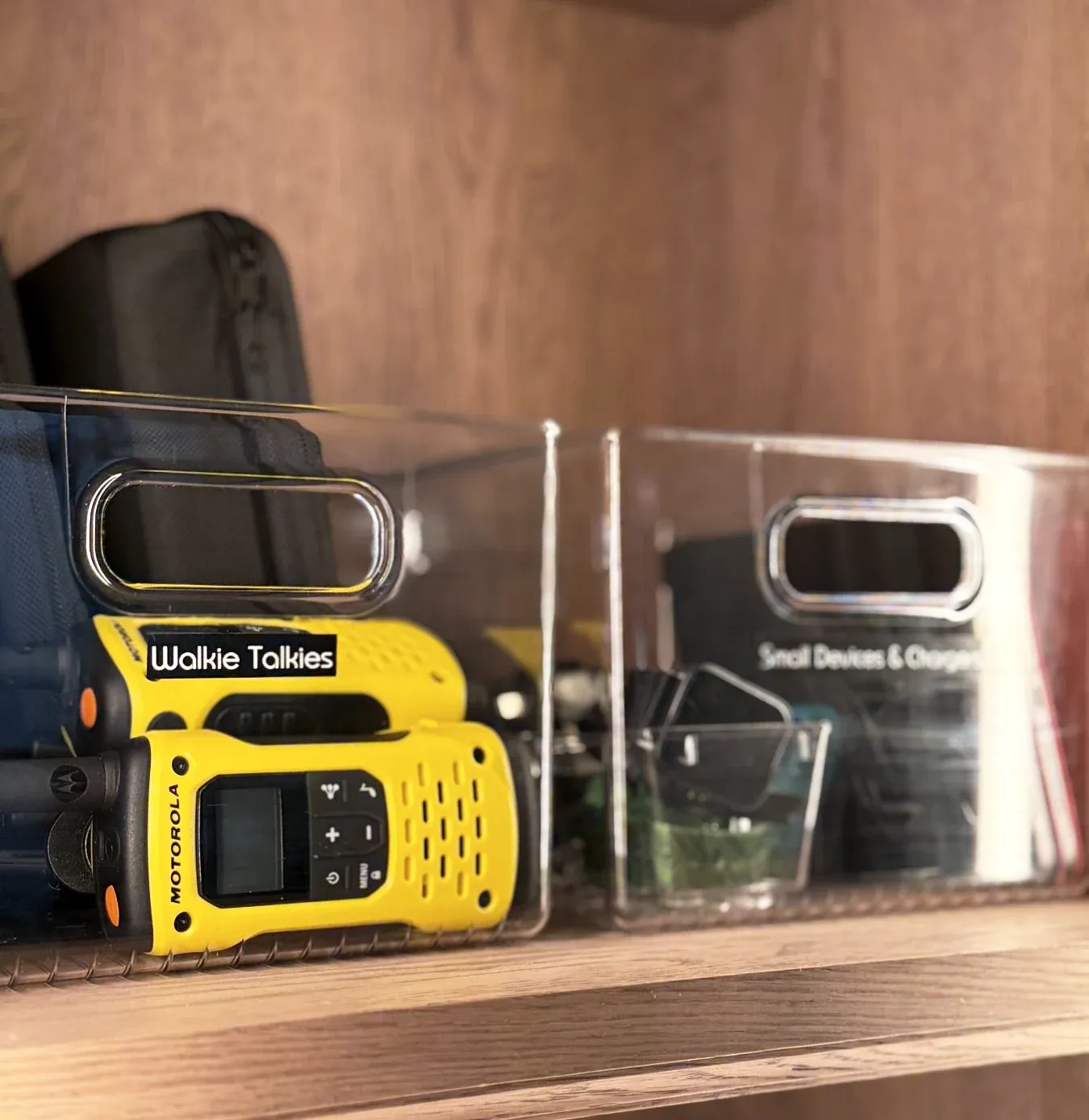 Walkie-talkies and a charger on a labelled shelf.