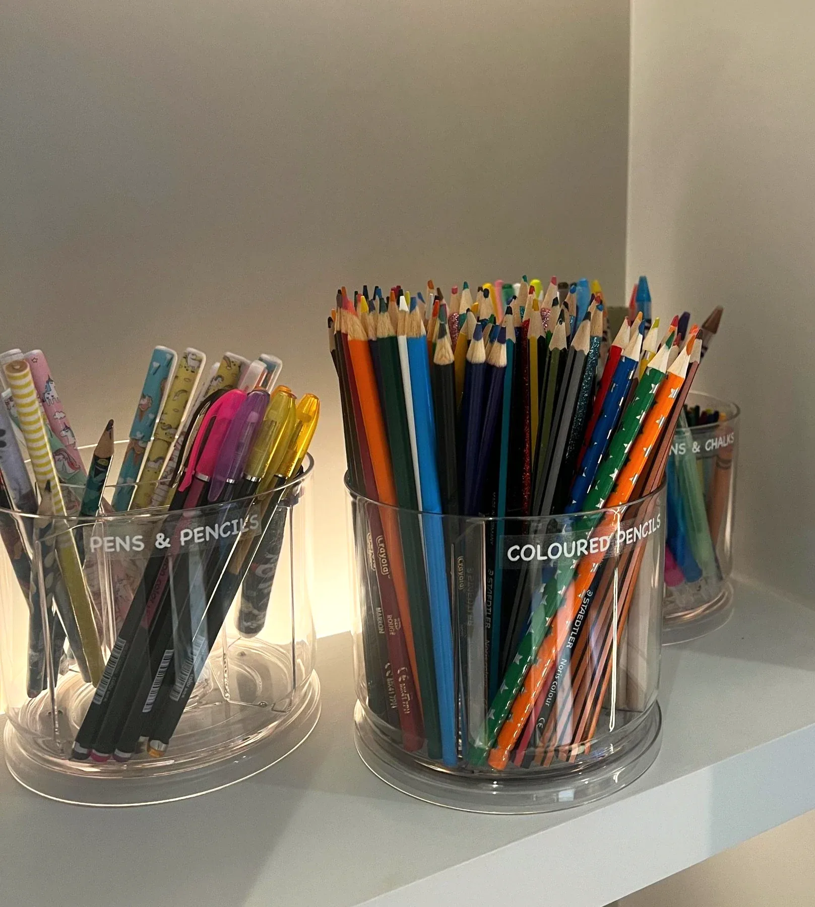 Pencils and pens sorted by colour into clear pots.