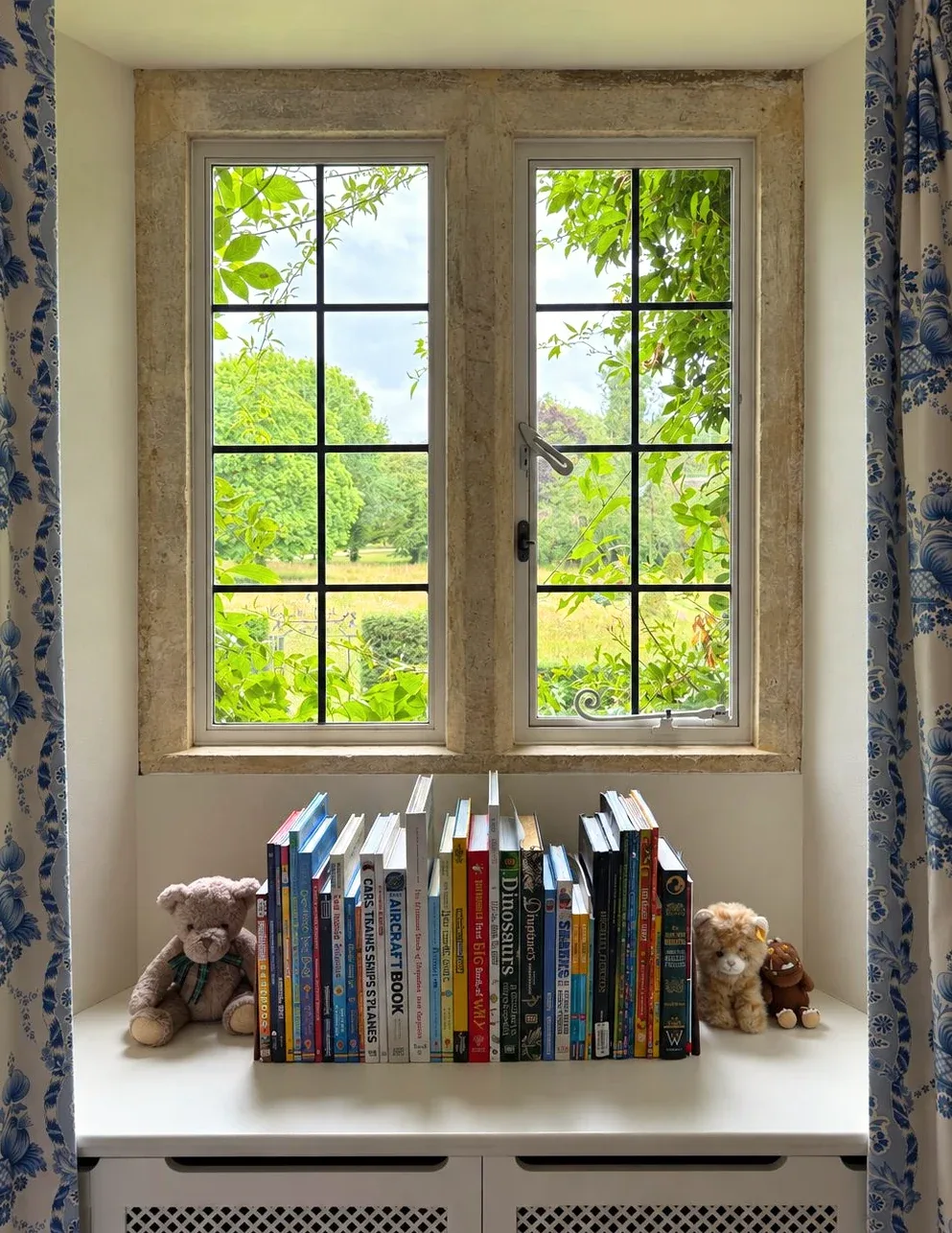 A window seat in a child's room, books along the sill and a garden beyond.