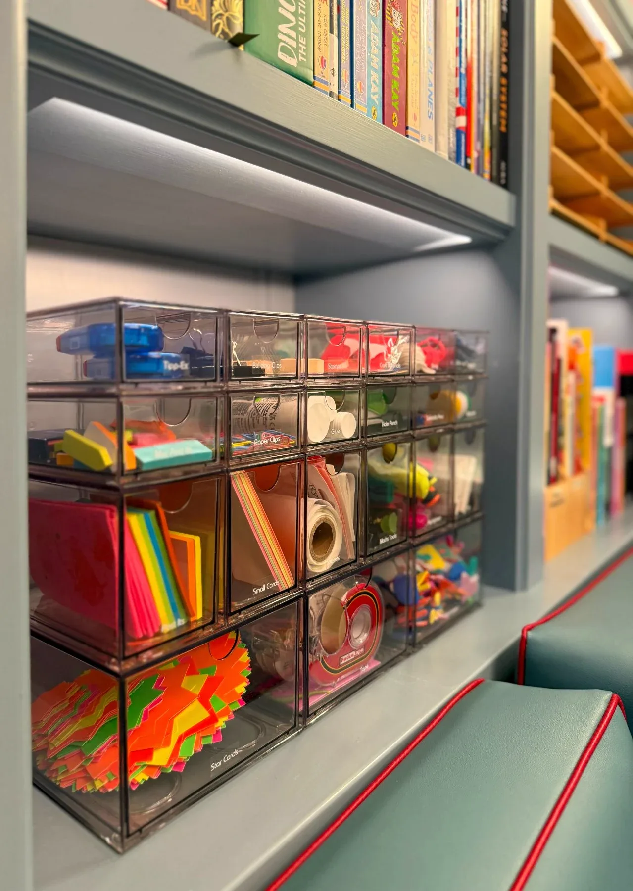 Clear boxes of craft materials on lit shelves beside books.