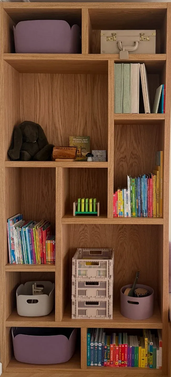 A timber unit of cubbies holding books and small toys.