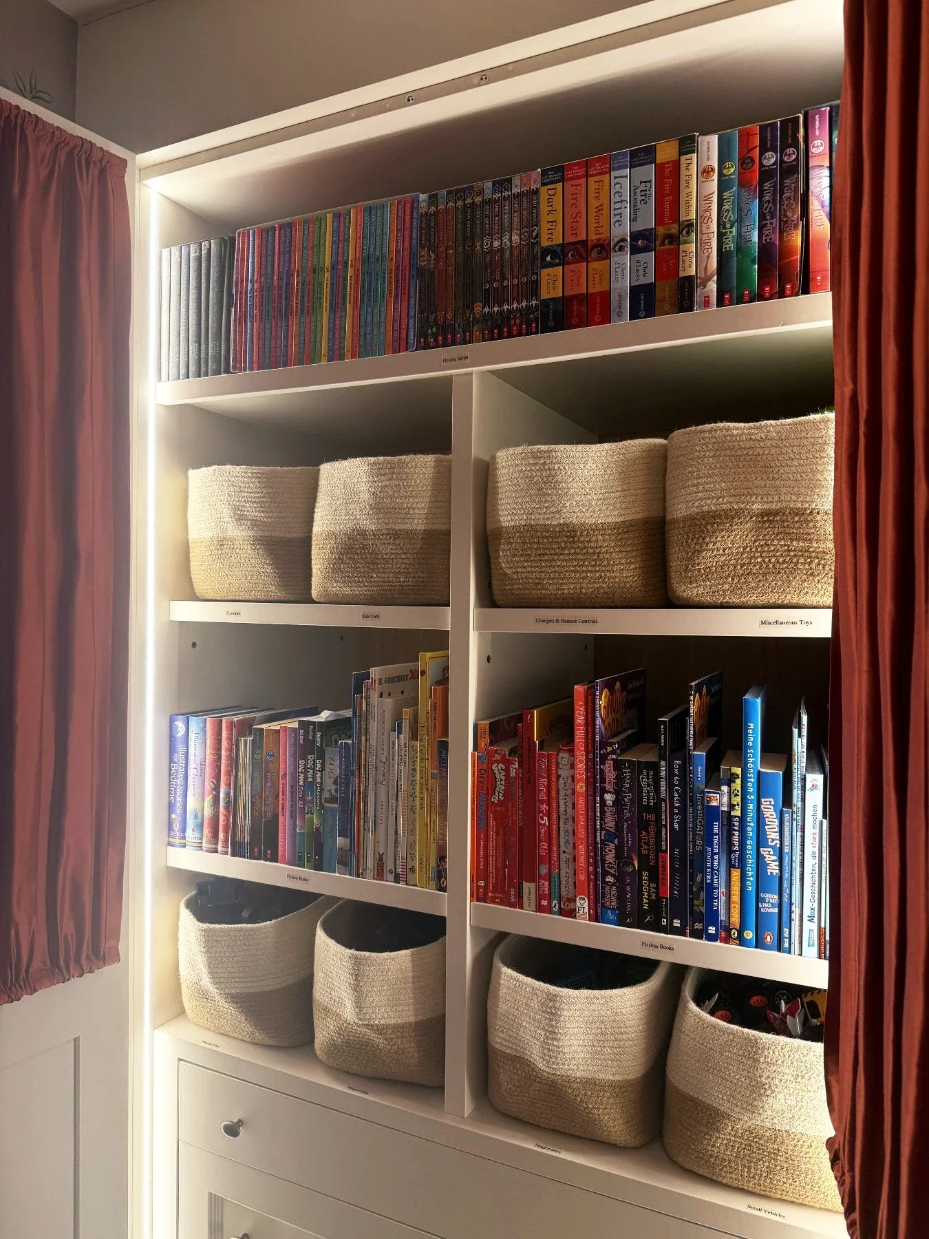 A bookcase of upright books with woven baskets below.