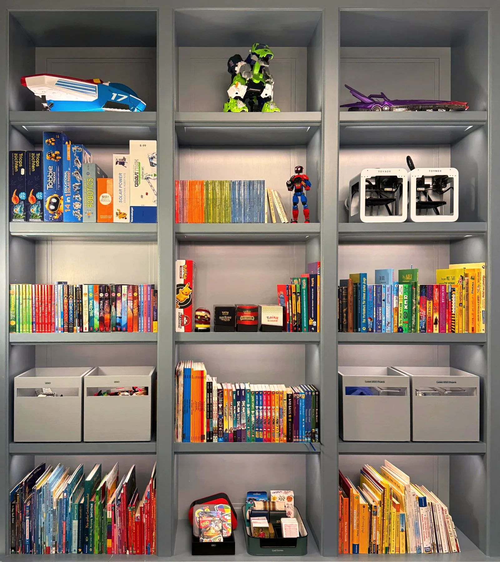A child's library wall of books, toys and fabric storage boxes in painted shelving.