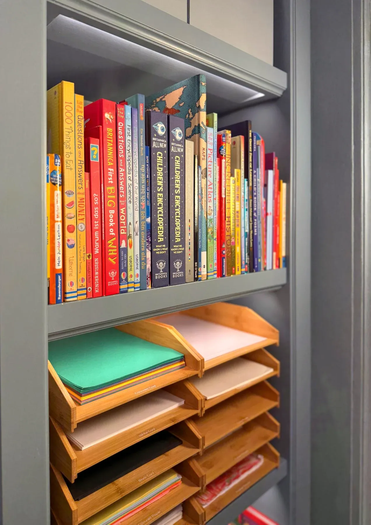 Children's books shelved above a stack of paper trays.