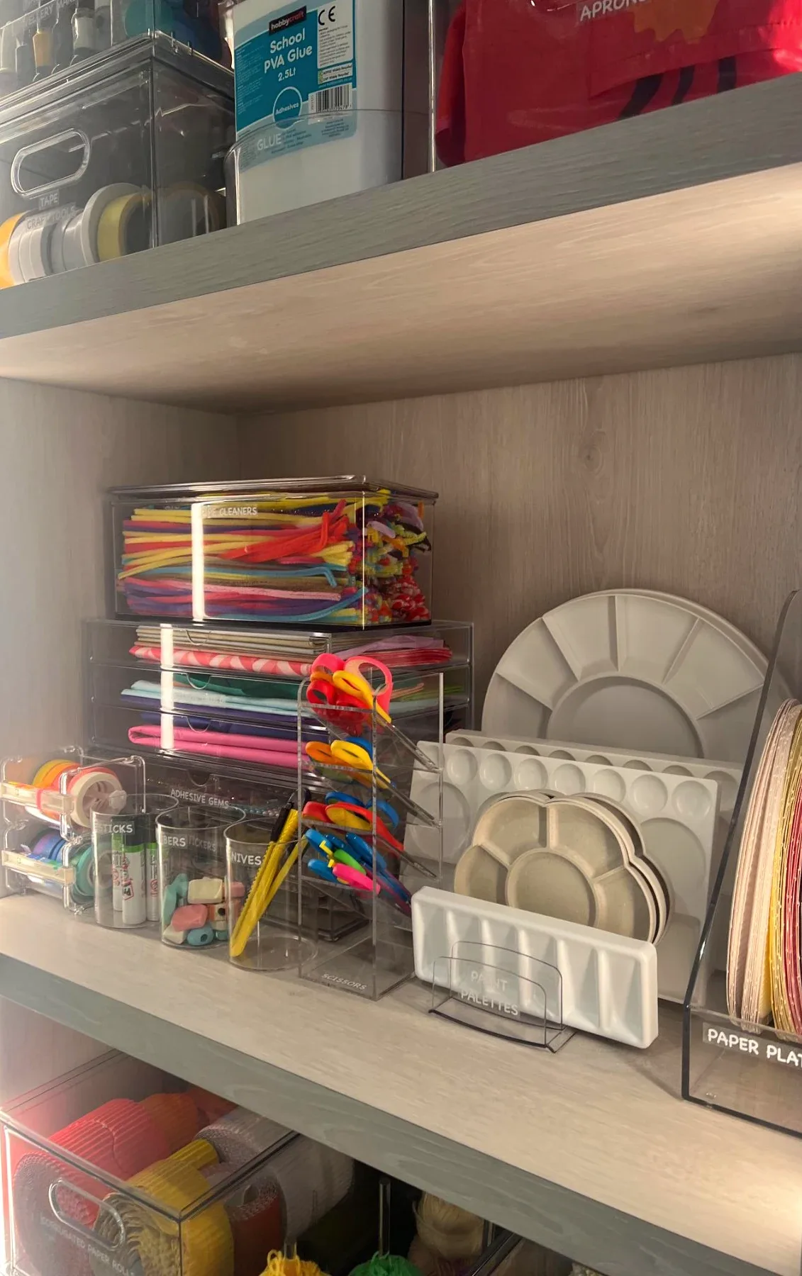 Craft materials and paper in clear trays on open shelves.
