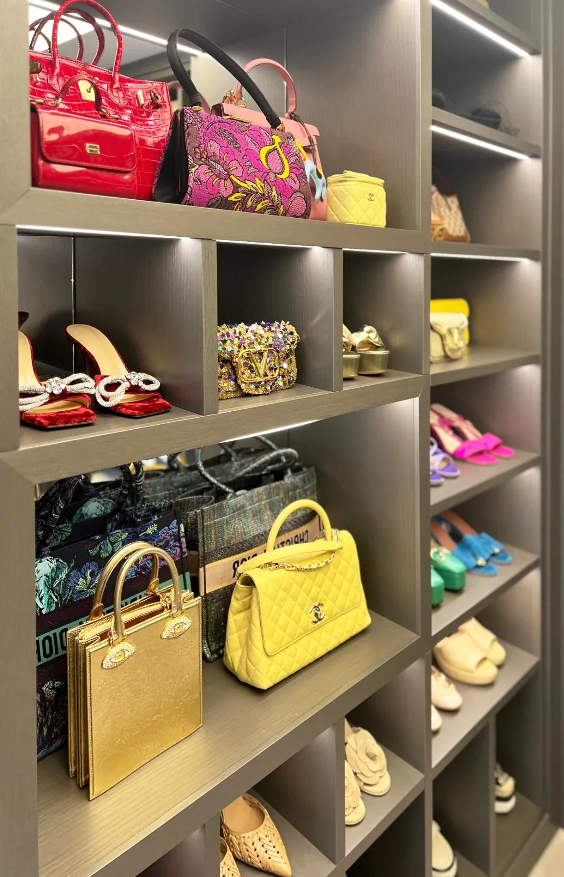 Handbags and shoes set out in lit open cubbies along a dressing room wall.