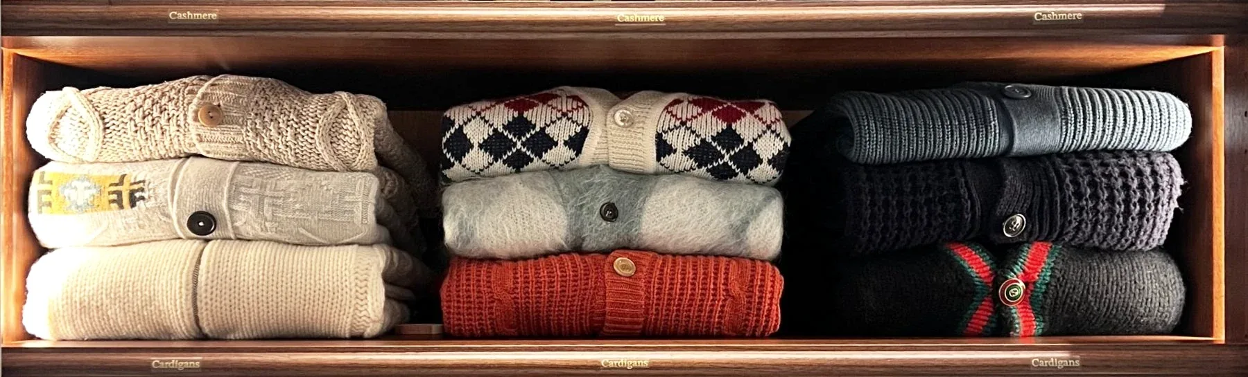 Three stacks of folded knitwear in one shelf bay, the shelf edges labelled by kind.