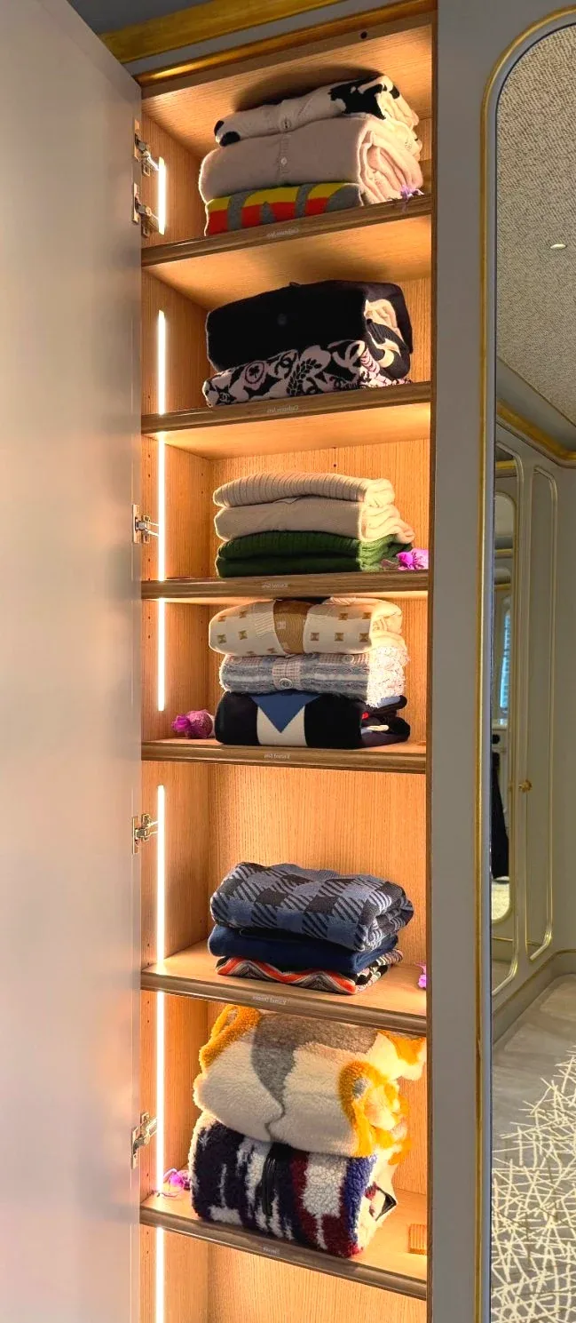 A narrow lit cabinet holding folded clothes and accessories.