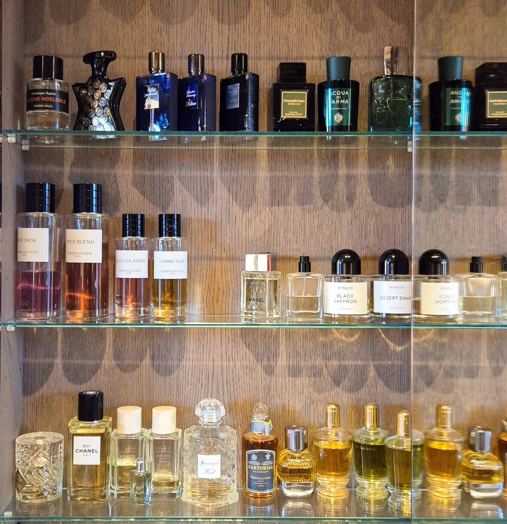 Scent bottles arranged along lit glass shelves.