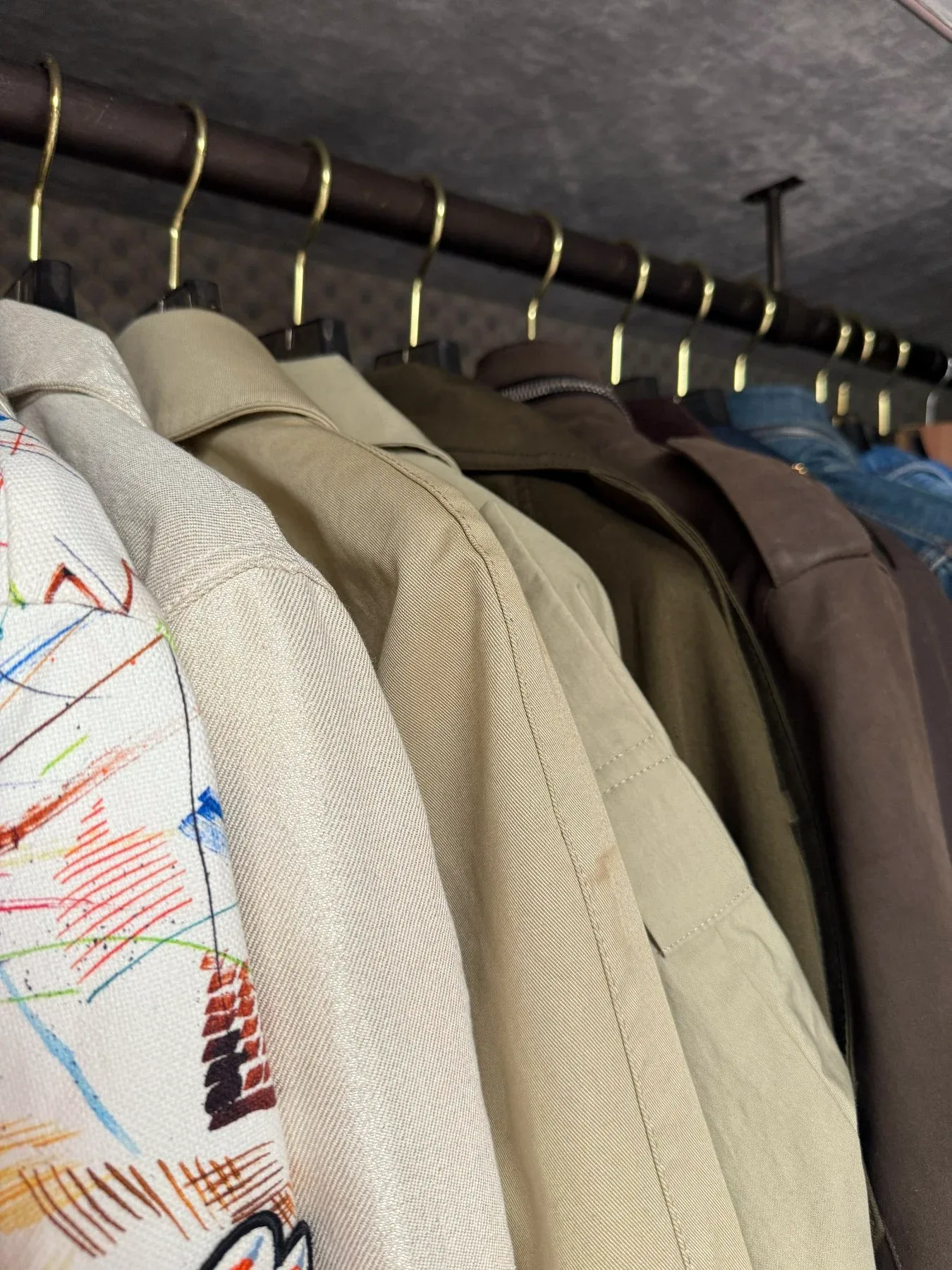Coats and jackets hanging closely together on a rail.