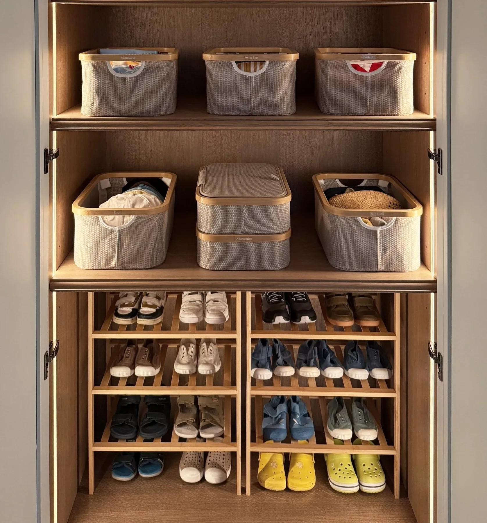 Fabric storage boxes above rows of shoes in a timber cupboard.