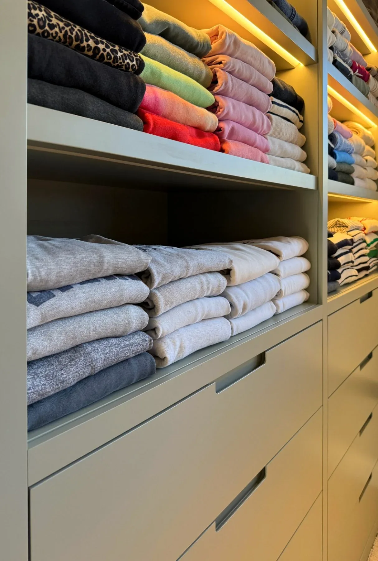 Folded towels and knitwear on lit shelves above drawers.