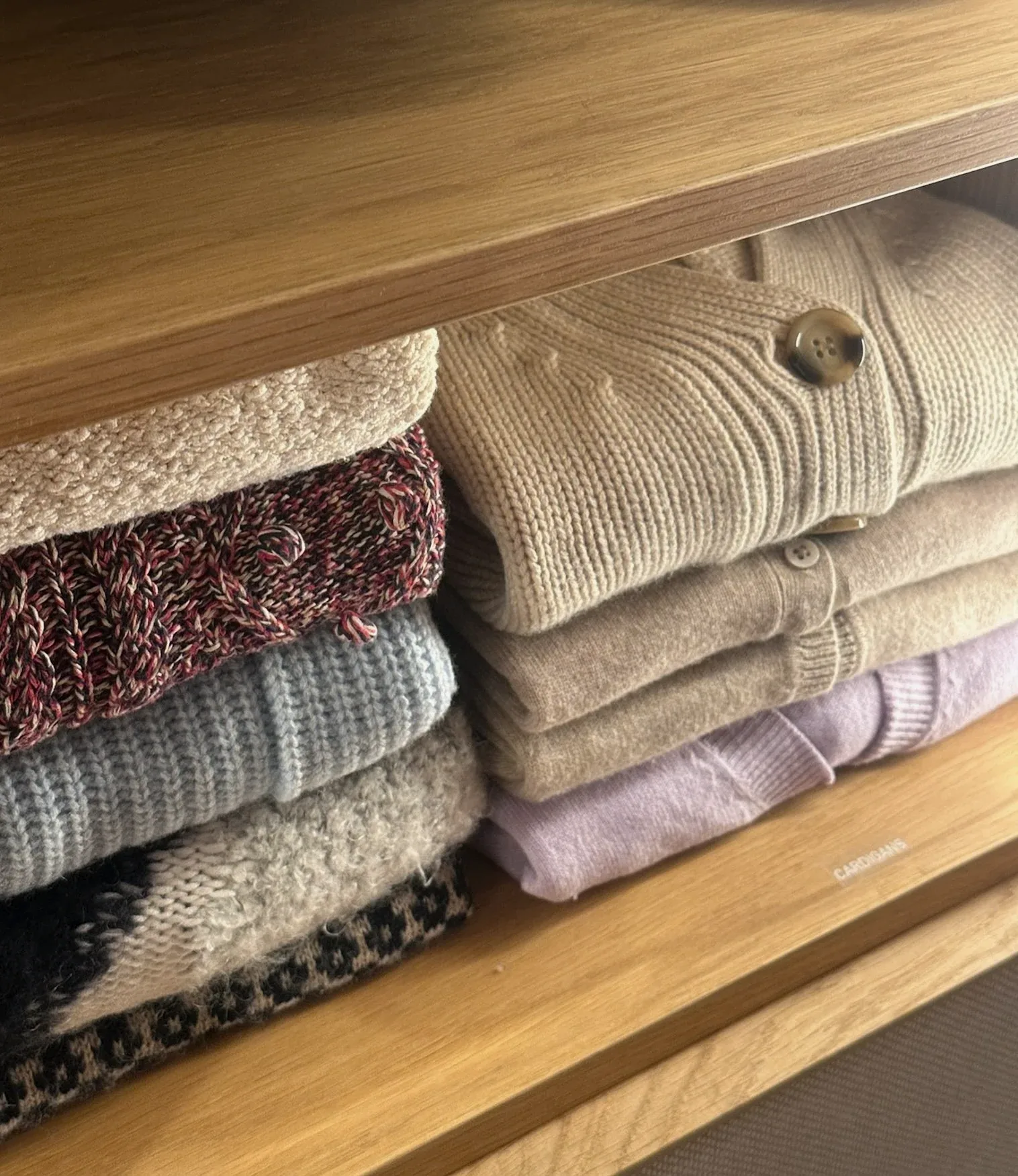 Folded knitwear in soft colours on a timber shelf.