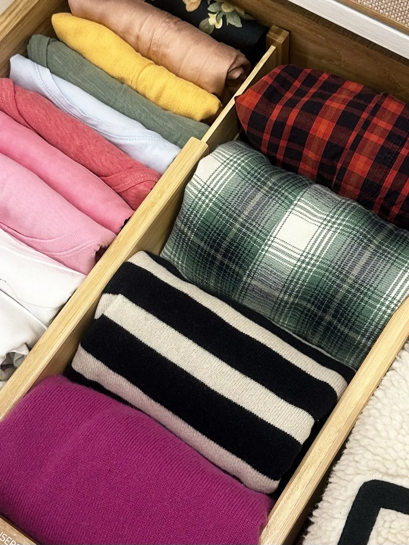 A drawer of folded clothes sorted by colour.