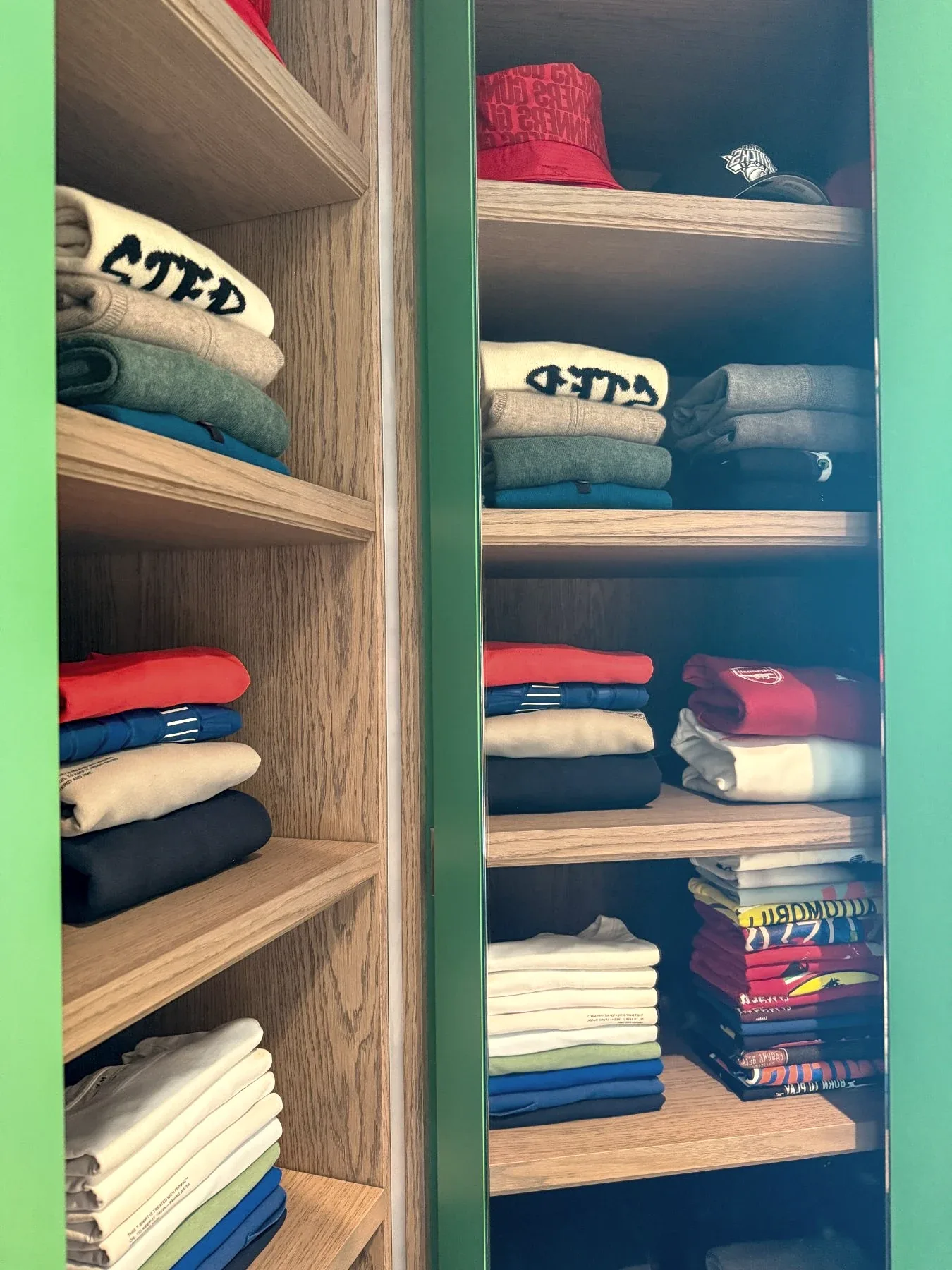 Folded knitwear and sweatshirts on the open shelves of a green-painted wardrobe.