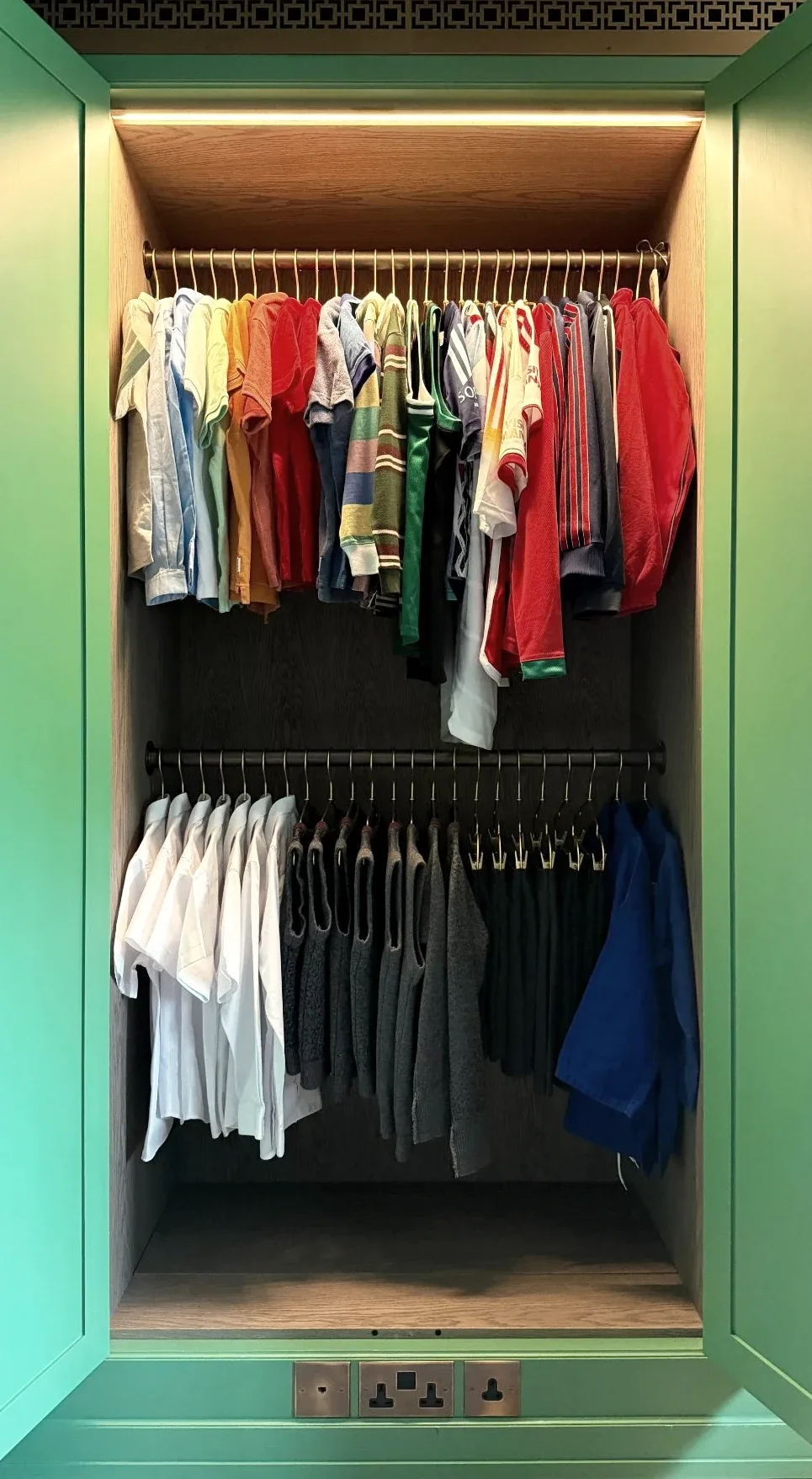 Shirts hanging on two rails inside a green-framed wardrobe.