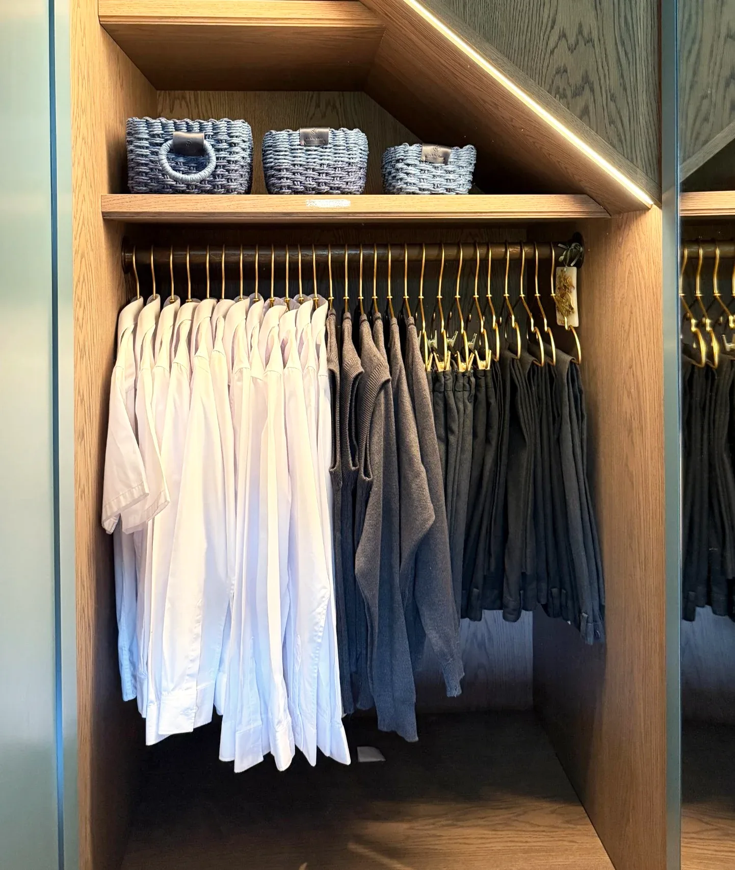 Shirts and trousers on a lit rail in a timber wardrobe.