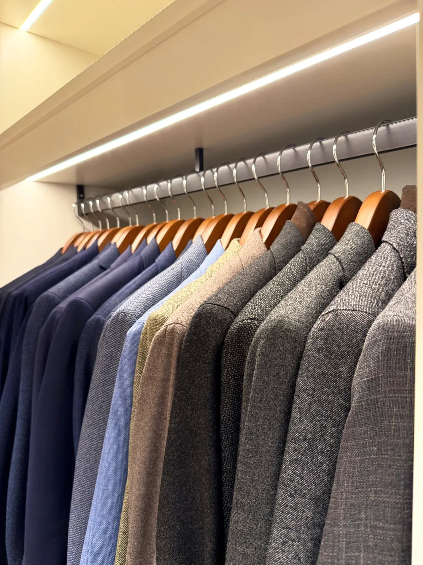 Suits and jackets graded from navy through grey on a lit rail.