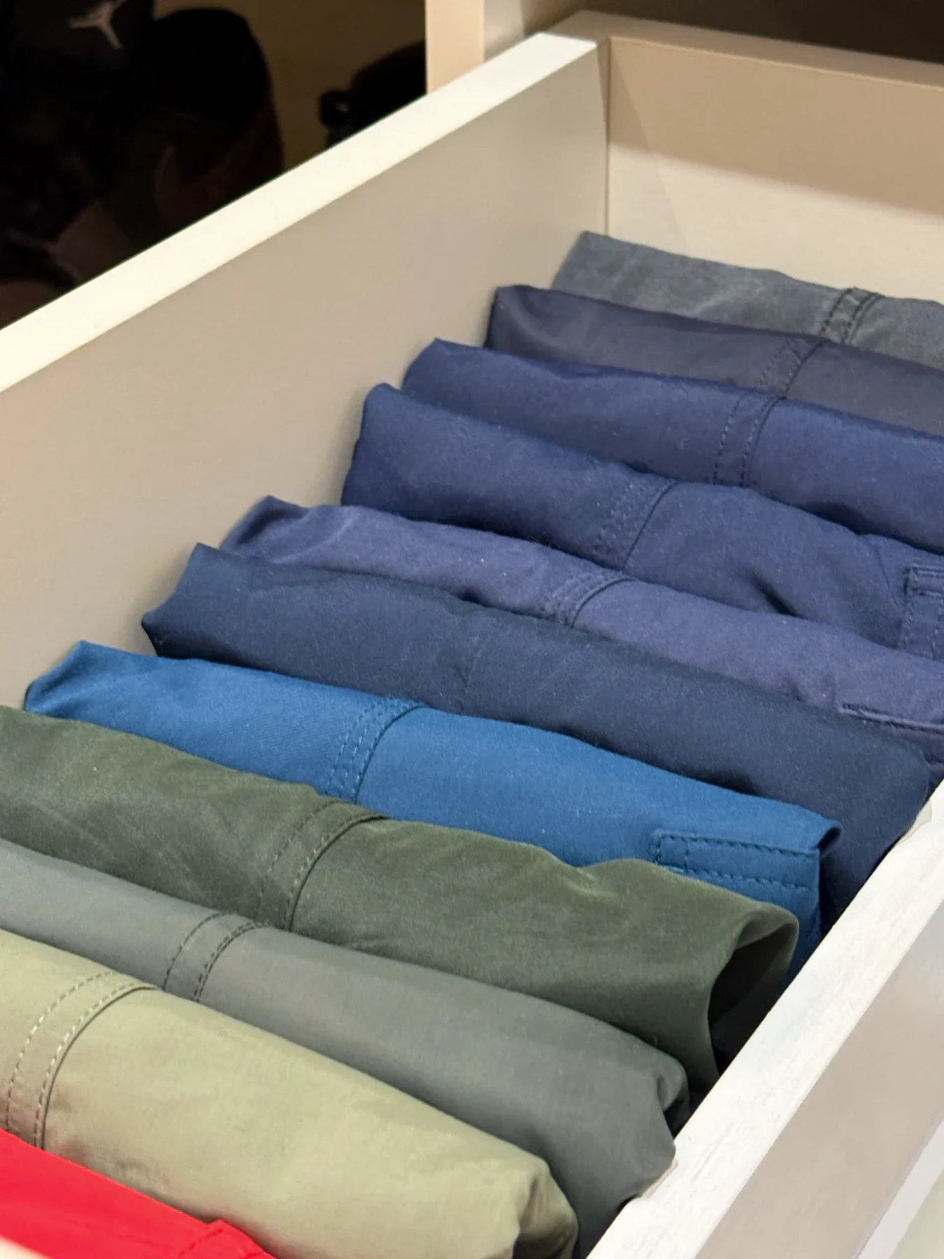 Folded jeans and trousers laid in a drawer by shade.