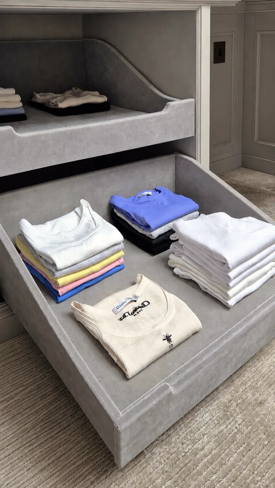 Folded T-shirts stacked in a grey drawer.