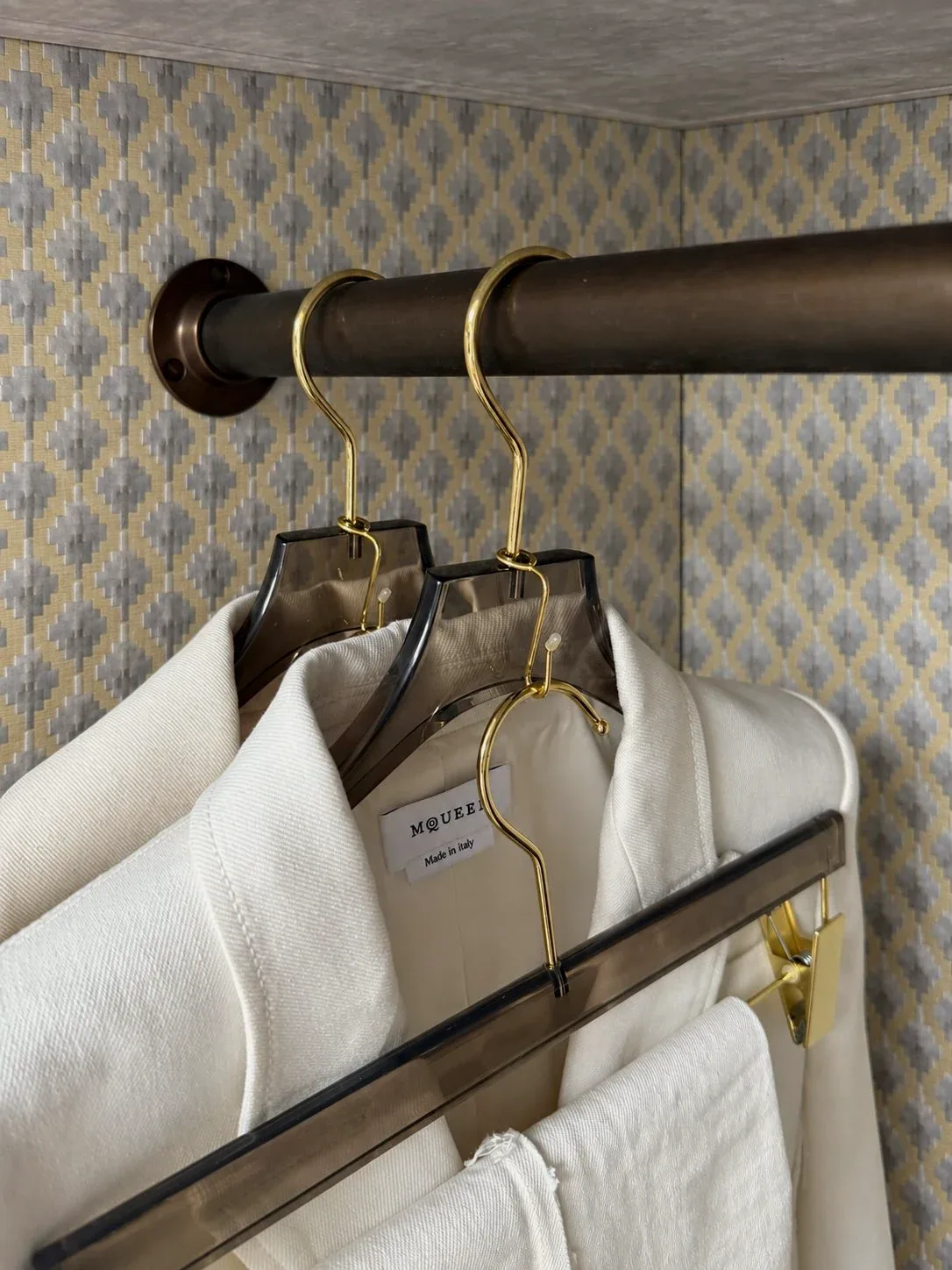Shirts on a rail against patterned wallpaper.