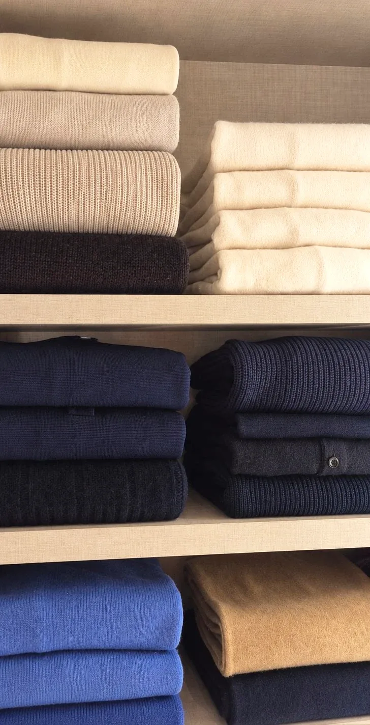 Folded knitwear above folded denim on open shelves.