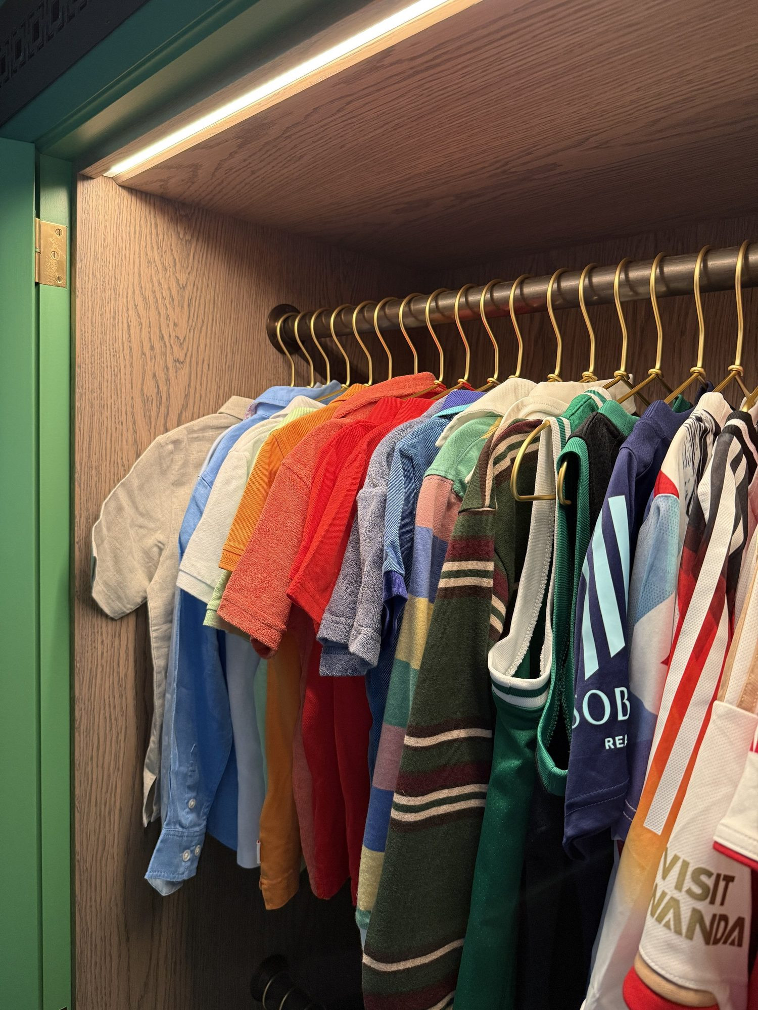 Children's clothes hung on a rail in a lit wardrobe.