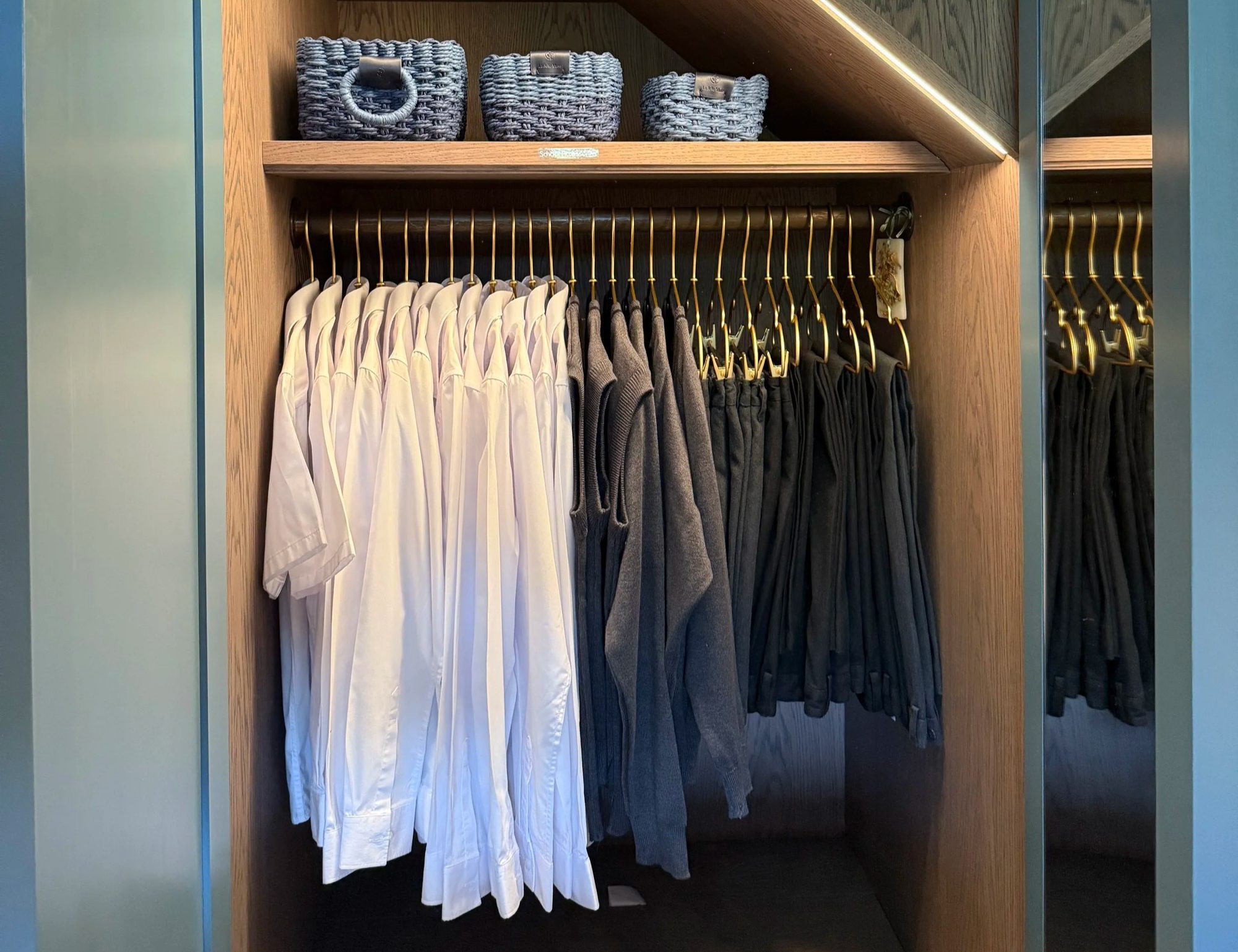 White shirts and dark trousers on rails in a fitted wardrobe, with woven baskets on the shelf above.
