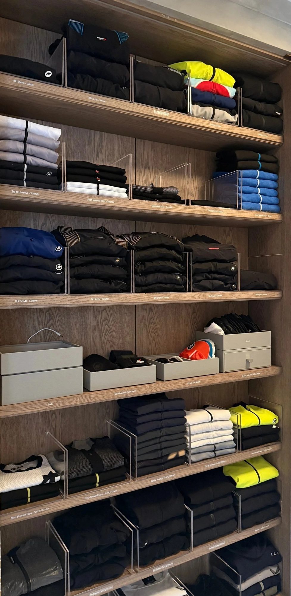 Folded clothing and storage boxes on tall wardrobe shelves.