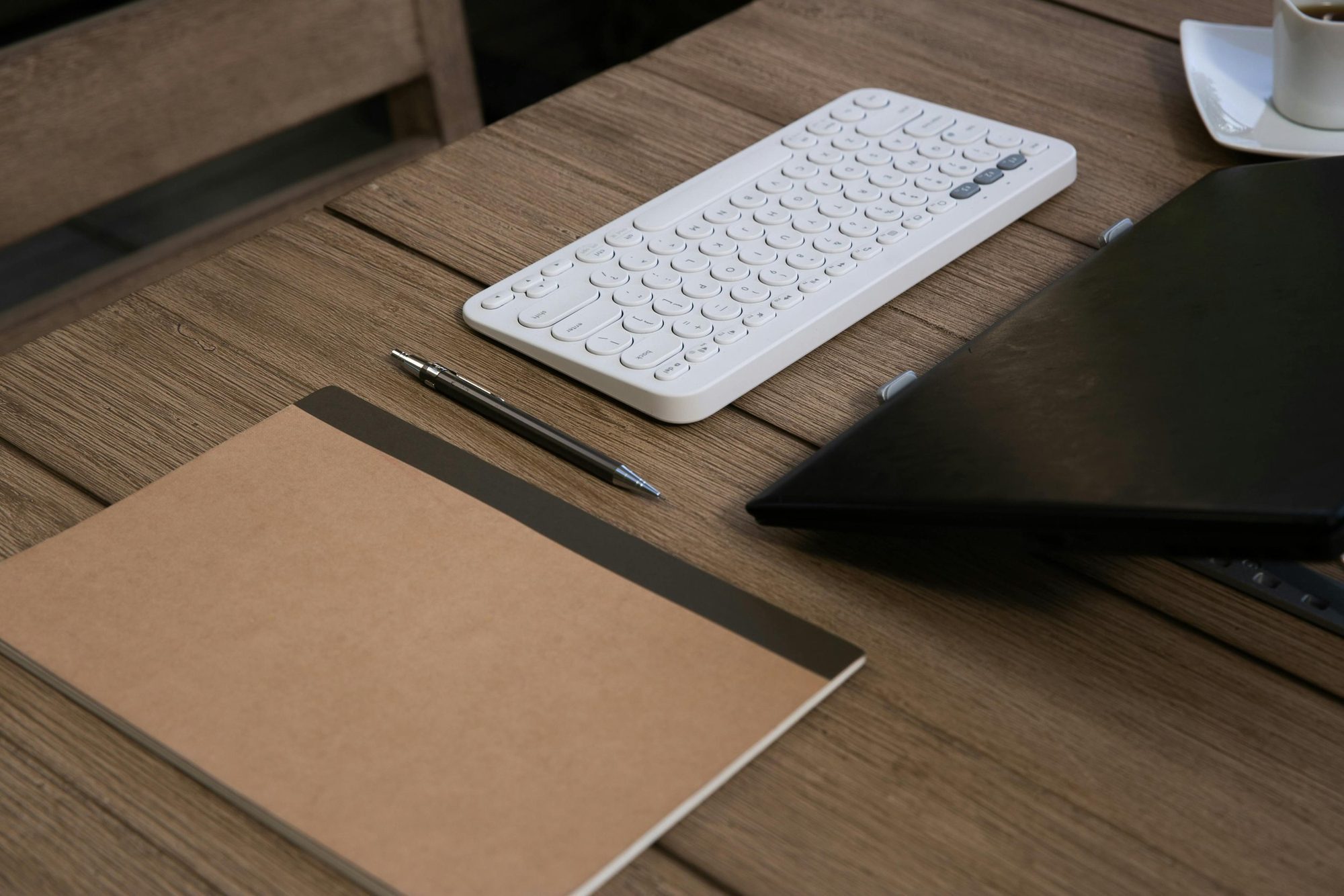 A keyboard, notebook and pen on a desk.