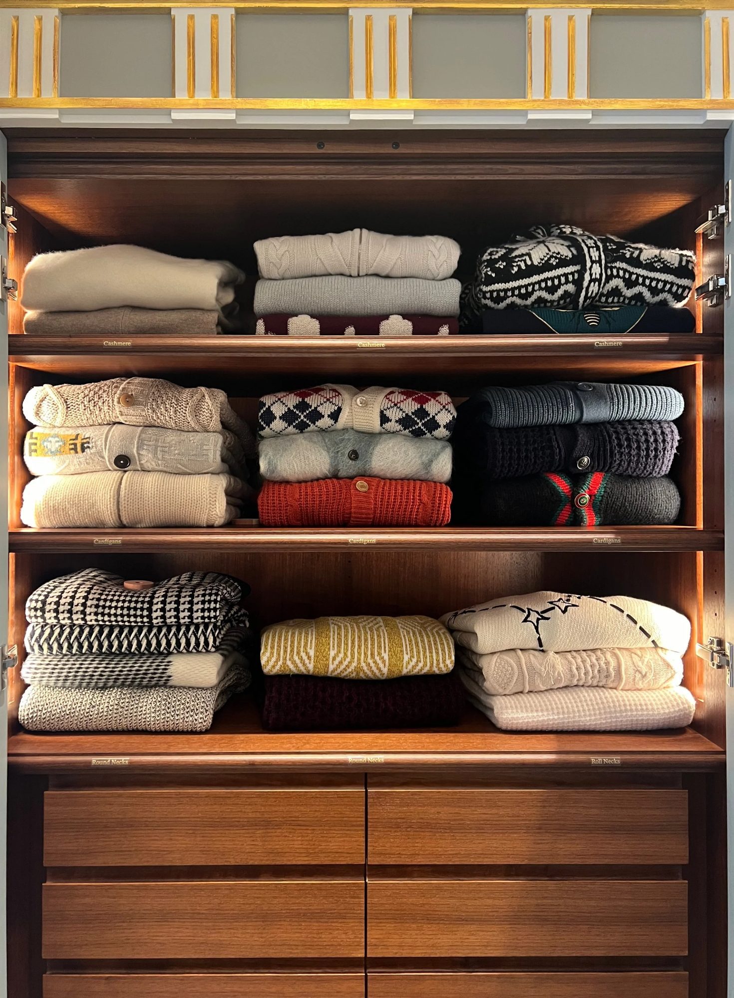 Knitwear folded in stacks on wardrobe shelves above drawers.