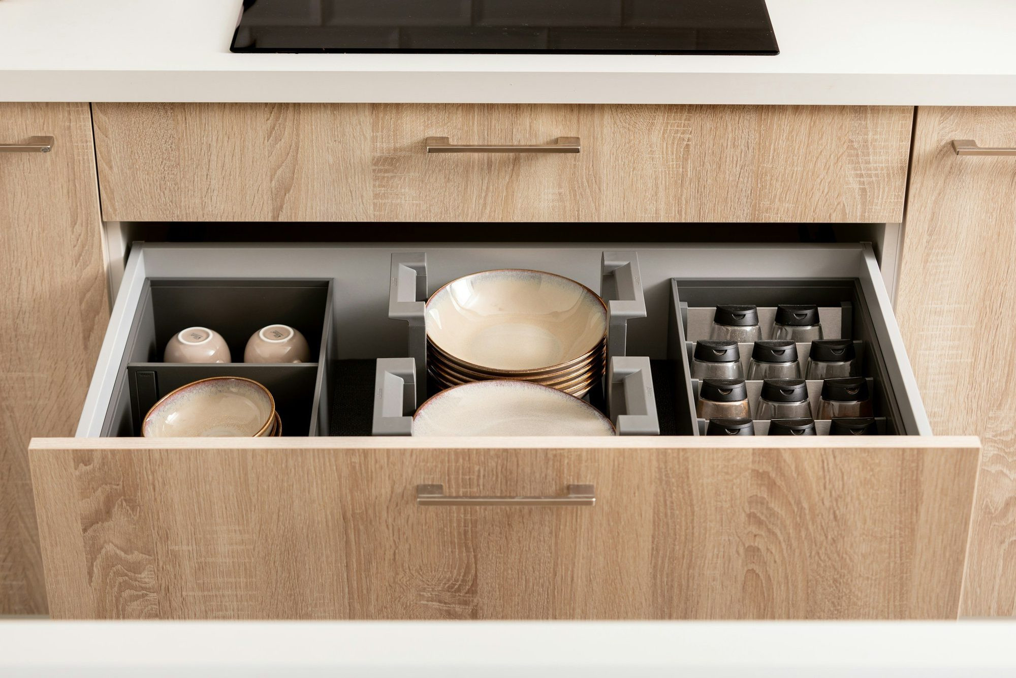 An open kitchen drawer with bowls and containers in fitted dividers.