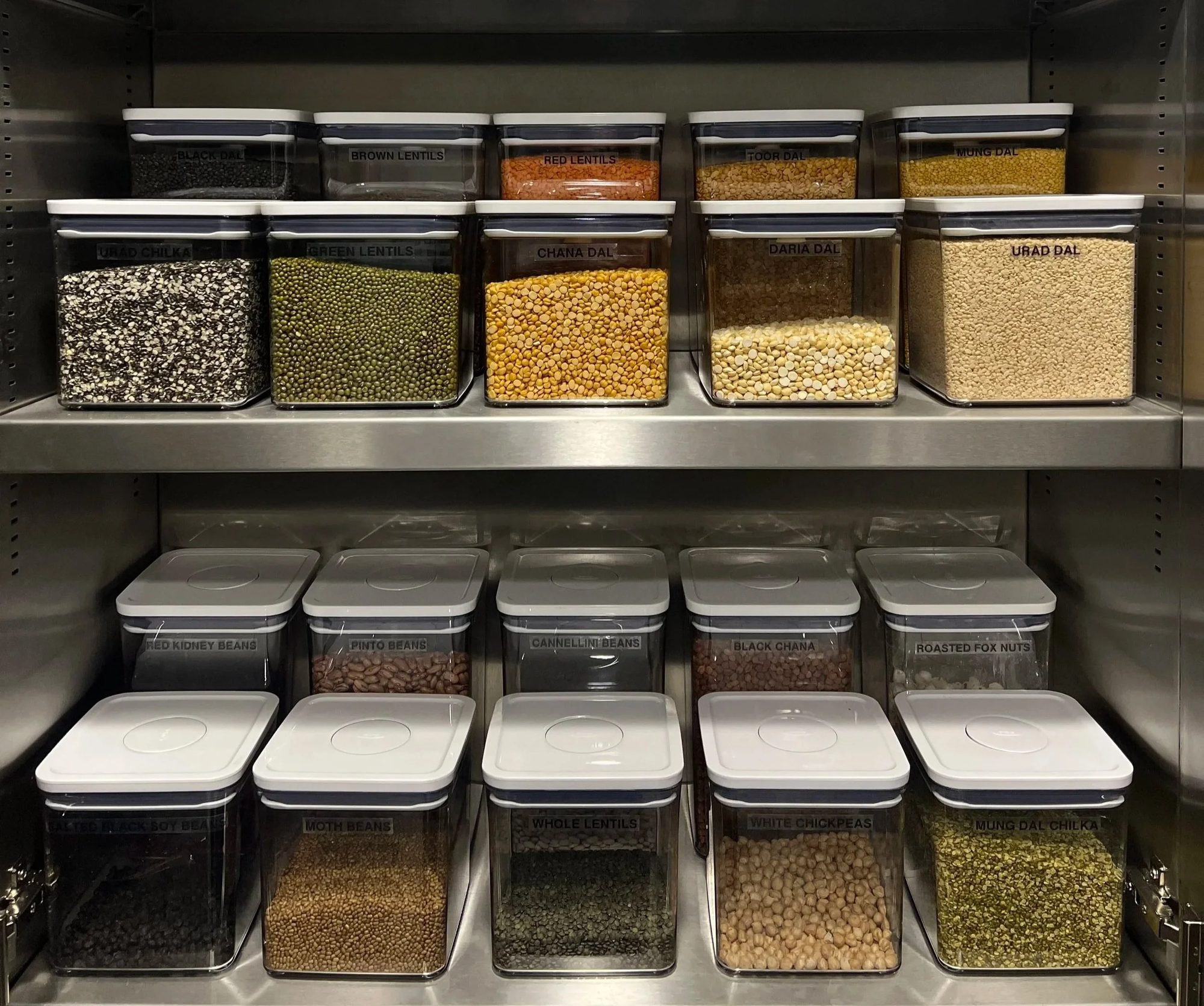 Dry goods in matching clear containers on pantry shelves.