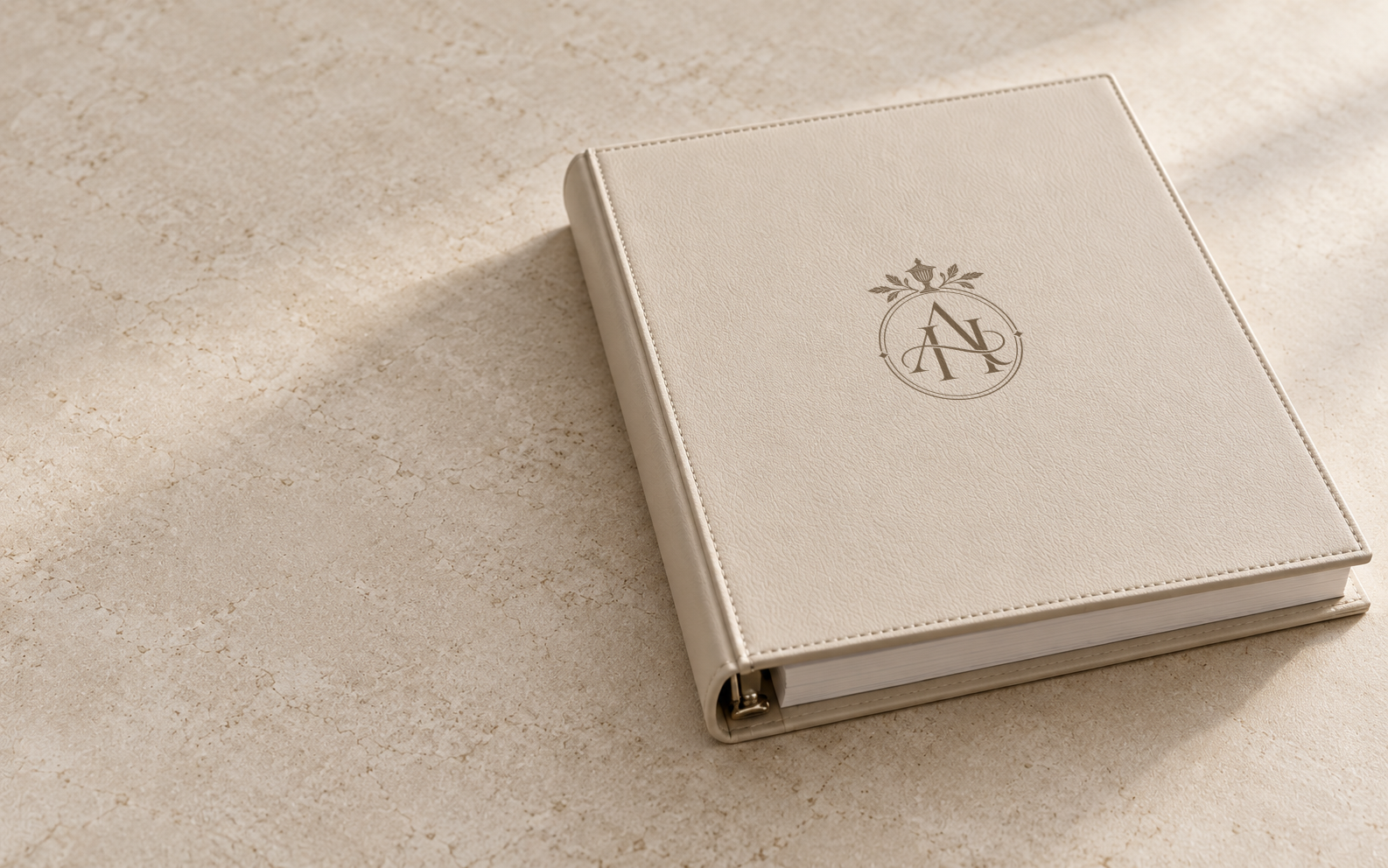 A closed household manual in a pale leather ring binder, its cover stamped with a monogram, on a stone surface.